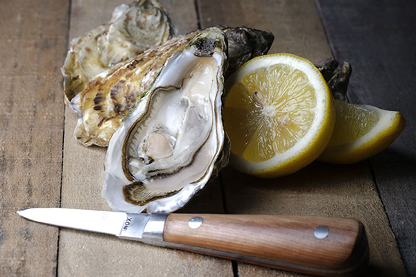 Un couteau à huîtres devant des huîtres et un citron